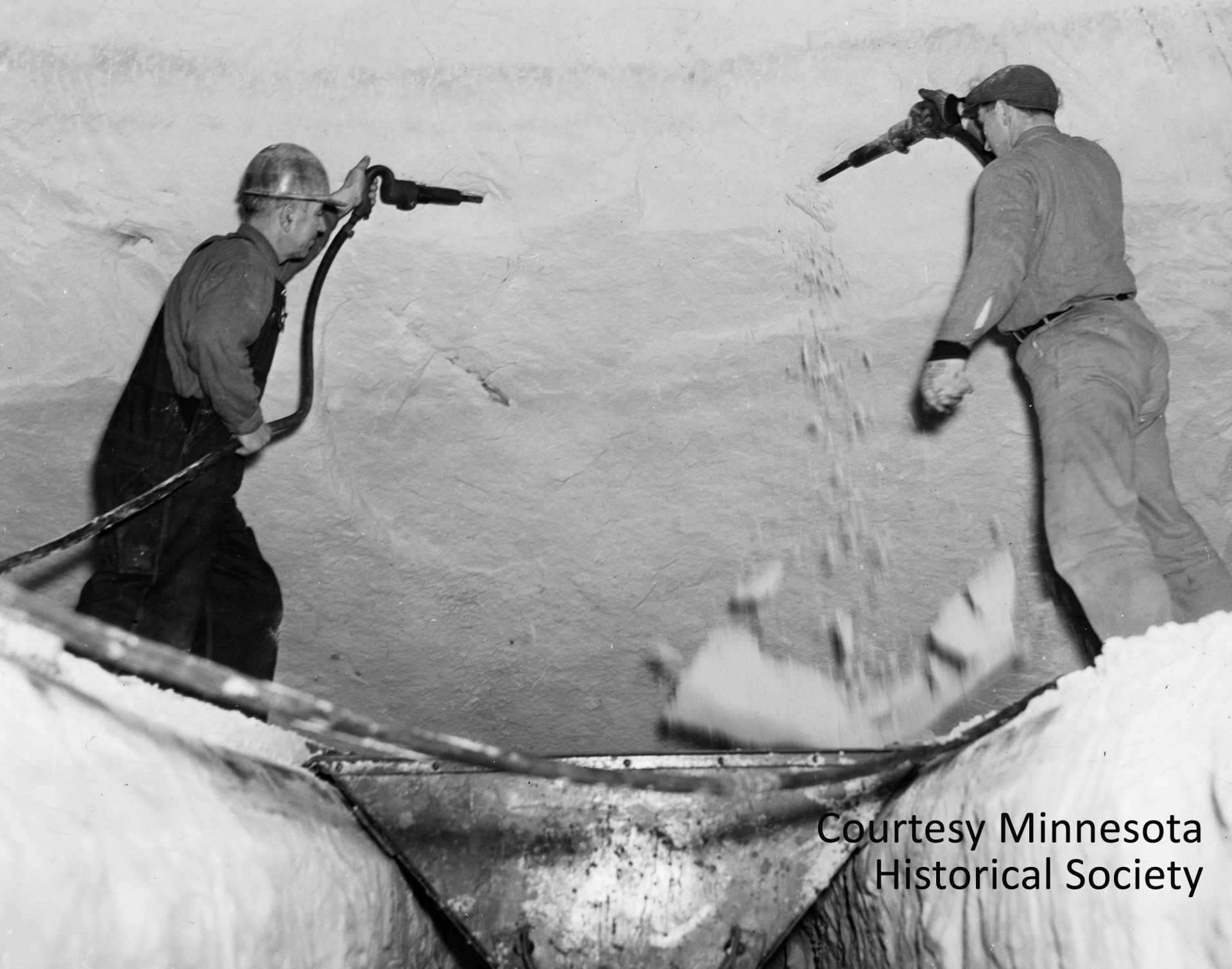 Workers used air guns to blast the silica sand out of the many tunnels that had been excavated 100 feet beneath the Ford plant. The sand was loaded into small electric carts and carried by conveyer up to the furnaces where it would be made into glass. Courtesy Minnesota Historical Society