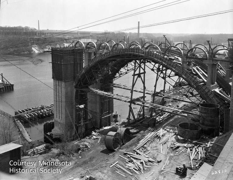 The Intercity Bridge, seen under construction in this 1926 photo, was one of the few bridges spanning the Mississippi that connected Minneapolis and Saint Paul. The Twin Cities Assembly Plant can be seen in the background. Courtesy Minnesota Historical Society